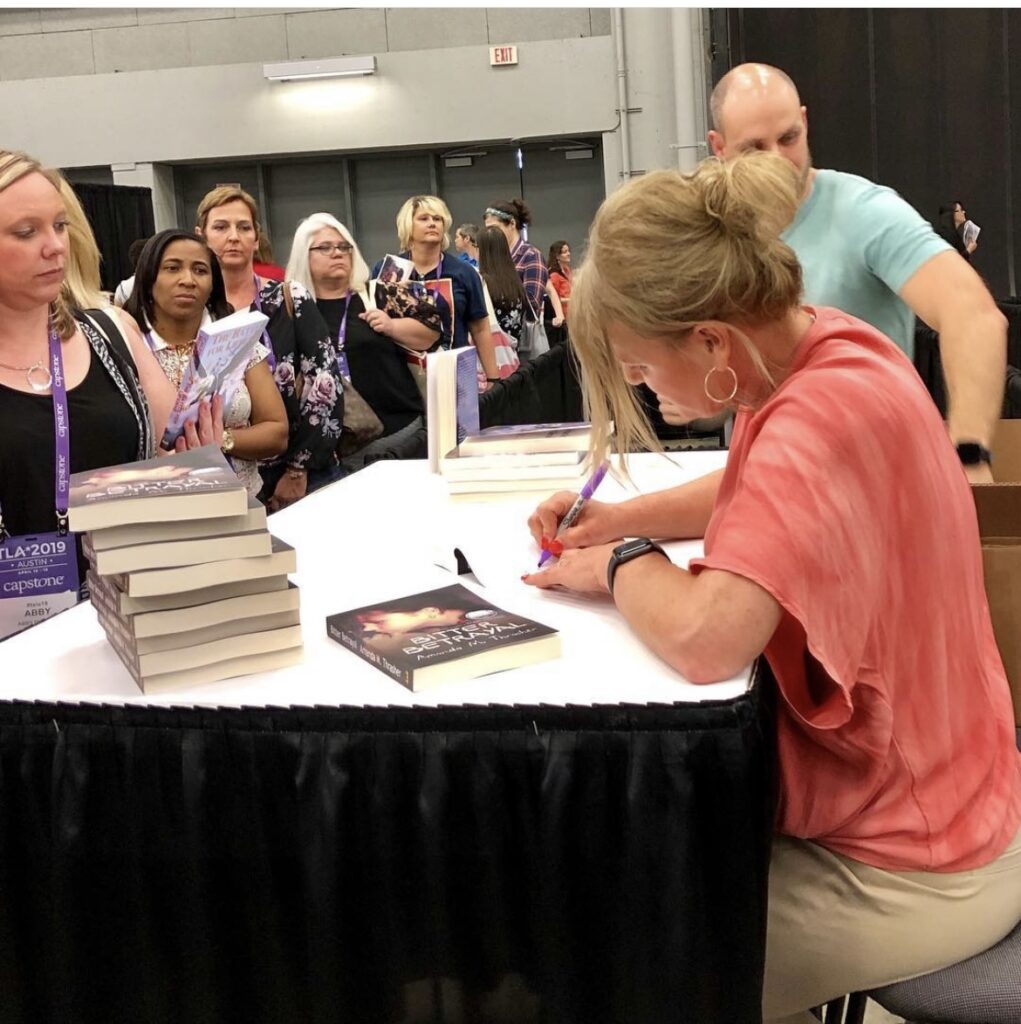A Woman in a Peach Color Shirt Signing a Book